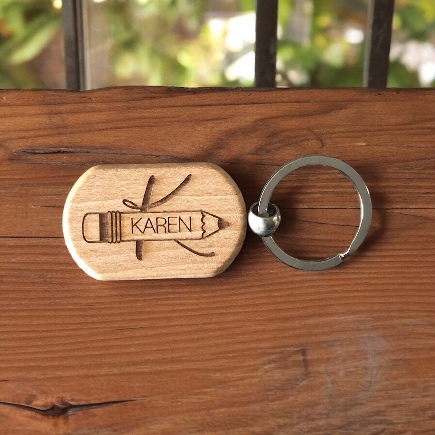 Wooden keychain on a wood table with metal ring attachment, Engraved pencil with teachers name inside
