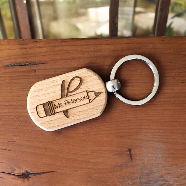 Wooden keychain on a wood table with metal ring attachment, Engraved pencil with teachers name inside